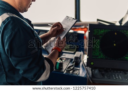 Marine navigational officer or chief mate on navigation watch on ship or vessel. He fills up checklist. Ship routine paperwork Royalty-Free Stock Photo #1225757410