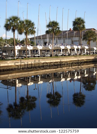 Ten sailboats on trailers reflected in a quiet channel.