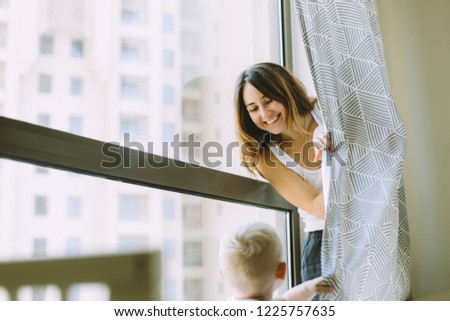 Mother playing with her little son in the bedroom at home. Mother hiding behind the curtain.
