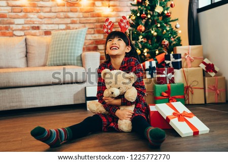 Sweet little girl hugging teddy bear looking up to sky smiling sitting on wooden floor. attractive childhood received gift on Christmas sale at home. kid with reindeer satisfied with present.