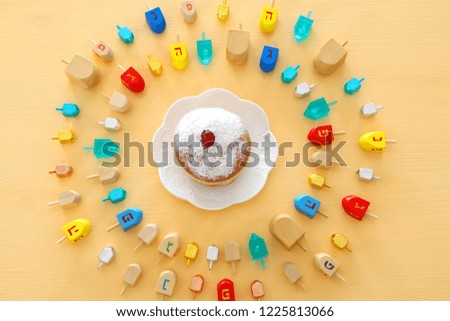 Image of jewish holiday Hanukkah with wooden dreidels colection (spinning top) and doughnut over pastel yellow background