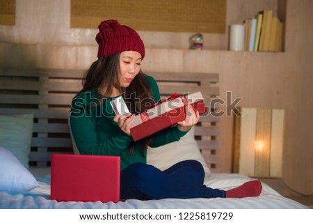 young beautiful and happy Asian Korean woman holding credit card and Christmas gift box shopping online xmas presents smiling satisfied at home bed  in e-business and e-commerce concept