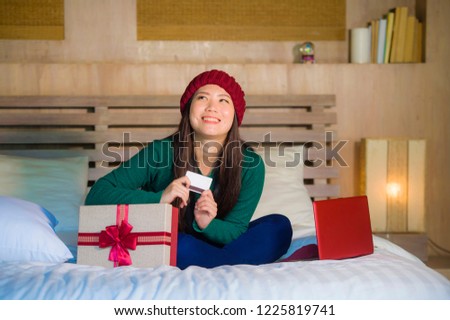 young beautiful and happy Asian Korean girl holding credit card and Christmas gift box shopping online xmas presents smiling satisfied at home bed  in e-business and e-commerce concept