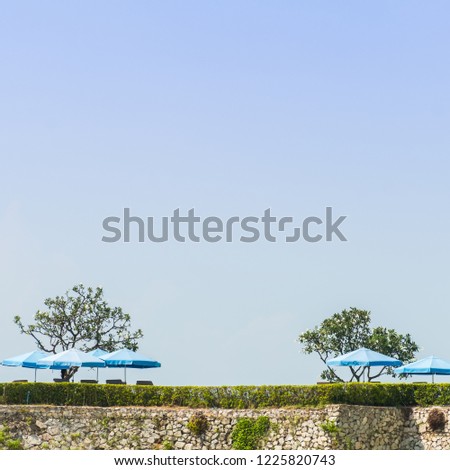 Beautiful blue umbrellas on the top of cliff for tourist sun bathing in tropical summer sea, minimalist picture style
