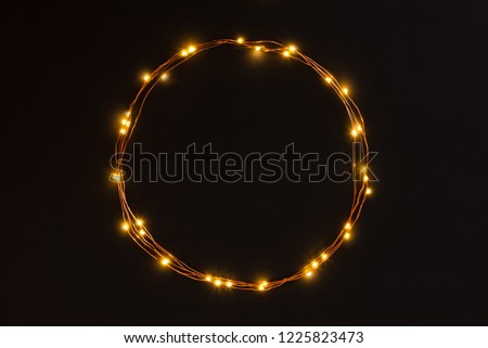 Christmas lights garland circular border over black background. Flat lay, copy space.