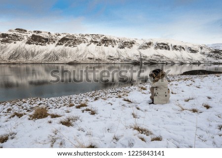 A female photographer taking a picture of a snow-covered mountain with reflections on the river in Iceland