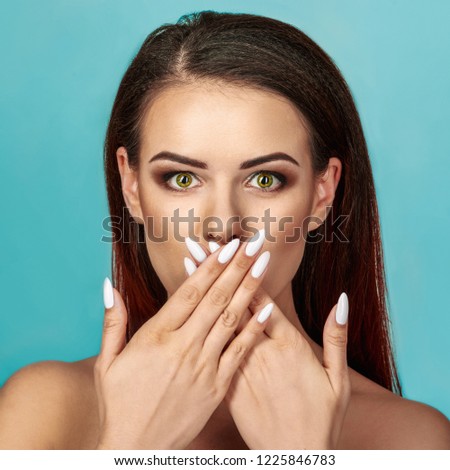 Portrait of beautiful young brunette woman covering mouth, on blue background