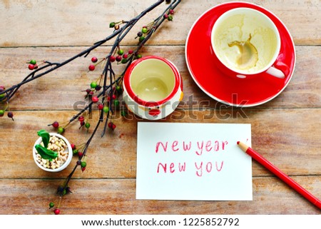 Drink coffee finished and write letter words New Year new you in white paper, red cup without drink, Santa claus cartoon cup, cactus in white pot, branch of berry on old wood board, Holidays concept 