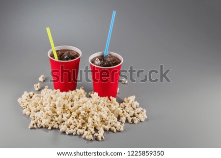 Closeup popcorn on the background of red plastic cups with fizzy drink with colored straws. Winter picture with snow.