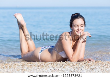 Young woman lying on front on pebbles near sea. Portrait of attractive girl in pale pink swimsuit