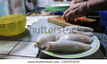 Some squid are stuffed in the foreground of the picture while the chef's hands are busy dicing tomatoes, out of focus, in the background.
