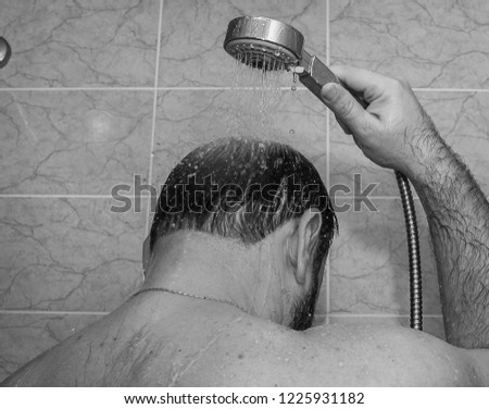 Black and white photo. A man pours water on his head from the shower.
