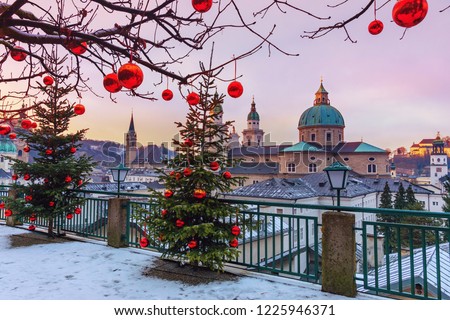 Beautiful view of the historic city of Salzburg with famous Salzburg Cathedral in winter, Austria.Christmas trees with red Christmas balls against the background of the winter Salzburg. Royalty-Free Stock Photo #1225946371