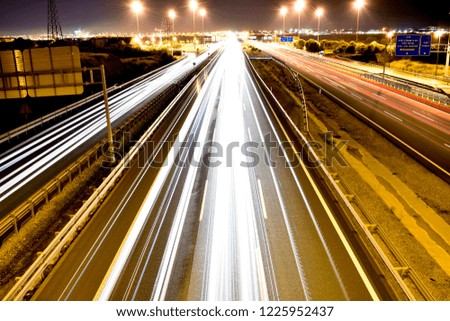 DIFFERENT WHITE, BLUE, YELLOW AND RED TRAFFIC LIGHTS OF MANY VEHICLES IN A SPANISH MOTORWAY WITH THE LIGHT OF A CITY AT THE END OF THE HORIZON