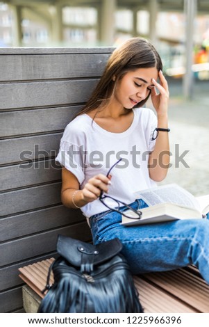 Young beautiful tired girl read a book sitting on a bench