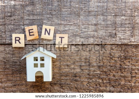 Miniature toy model house with inscription RENT letters word on wooden backdrop. Eco Village, abstract environmental background. Real estate mortgage property insurance sweet home ecology rent concept