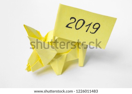 Yellow pig holds flag with inscription 2019. Swine of colored paper, origami. A cute animal. Festive mood, Christmas and New Year. Copy space, place for text.