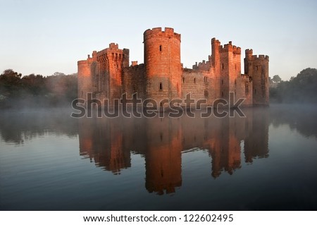 Beautiful medieval castle and moat at sunrise with mist over moat and sunlight behind castle Royalty-Free Stock Photo #122602495
