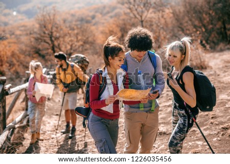 Hikers looking at map while standing on the glade. In background their friends walking. Autumn season, adventure concept.
