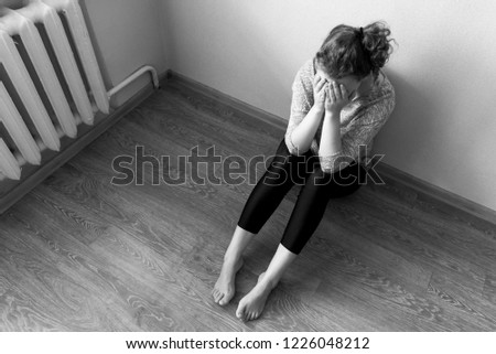 The girl is sitting on the floor and crying covering her face with her hands, black and white photo