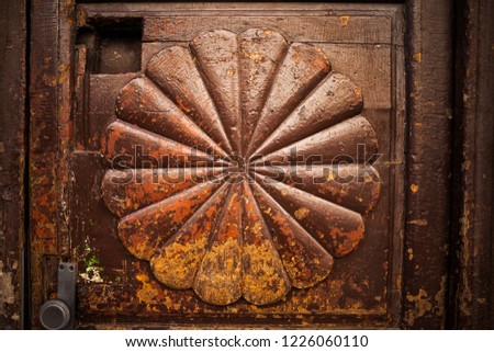 Vintage wooden door with abstract radial fan shape or flower petals, retro grunge look, peeling and flaking brown paint with yellow and orange accents.