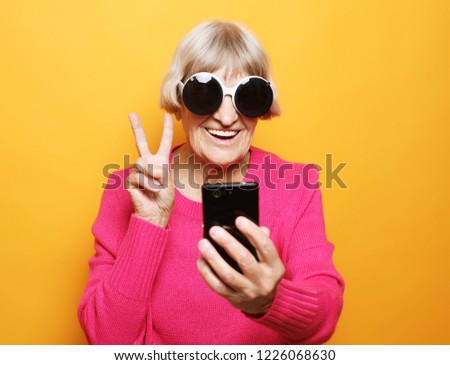 lifestyle, tehnology  and people concept: Elderly lady holding  a smartphone and making v-sign 