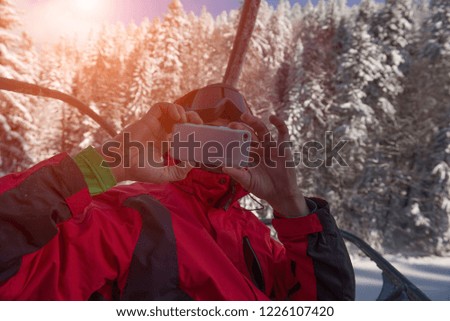 Teenager taking photo with smartphone from ski lift in winter mountains