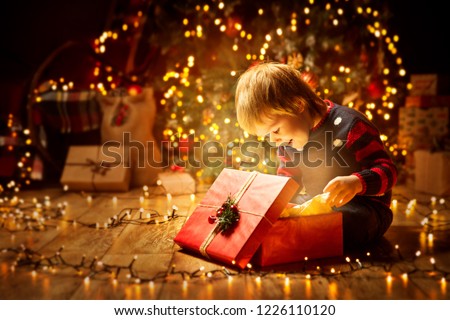 Christmas Child Open Present Gift, Happy Baby Boy looking to Magic Light in Box, Kid sitting front of Xmas Tree Royalty-Free Stock Photo #1226110120