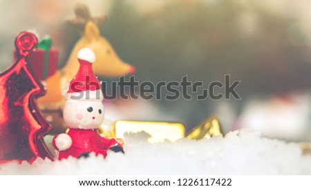 Traditional holiday decorations Concept. Close-up of Santa Claus made form wooden sitting on snow between colorful Christmas decoration and blurred Christmas tree with sunlight. Vintage style.