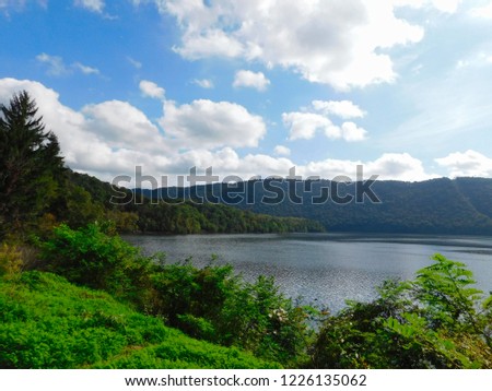 Image of Lake Raystown near Route 994 with the Appalachian Mountains in the background and green vegetation in the foreground.  Picture take in early fall in Pennsylvania.  Bright puffy clouds in sky.