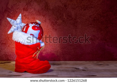 Red boot with Christmas tree ball and star on a wooden board before a red wall