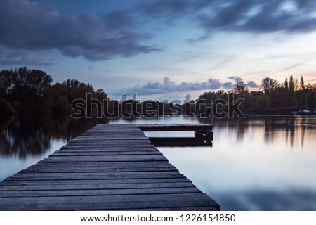 L shaped wooden jetty at evening twilight sky and long exposure blurry dramatic weather clouds. Südsee in Braunschweig, Germany