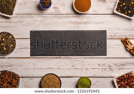 From above frame of different kinds of spice in small plates with black slate board in center on white wooden background