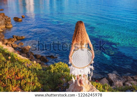 Bohemian girl with long red hair standing on the beach  holding dreamcatcher in white dress.