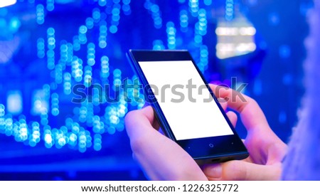 Woman looking at vertical smartphone with white blank screen at modern scifi technology exhibition. Blue abstract bokeh background. Mock-up, furute, sci-fi, template and technology concept