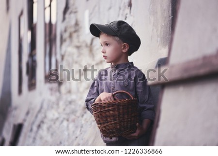 A sad, lonely boy on the street of the old town. Retro style. Pictures for the book's cover. A lost, waif child.