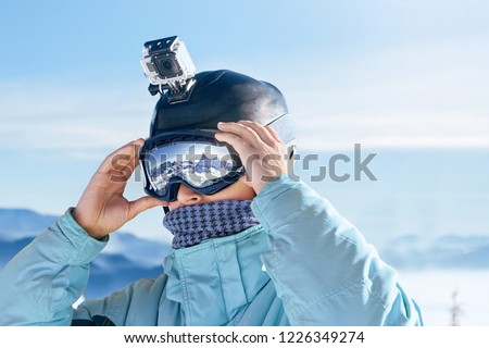 Skier with action camera on a helmet. Ski goggles  with the reflection of snowed mountains. Portrait of man at the ski resort on the background of mountains and blue sky,. Wearing ski glasses Royalty-Free Stock Photo #1226349274