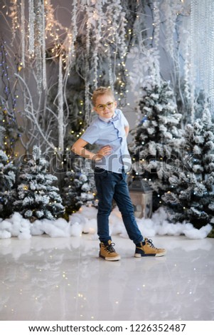 Christmas portrait of happy child boy with big glasses holding toy bear indoor studio, snowy winter decorated tree on background. New Year Holidays.