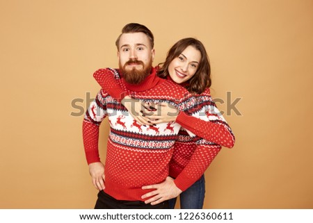 Happy girl and a guy dressed in red and white sweaters with deer are hugging on a beige background in the studio