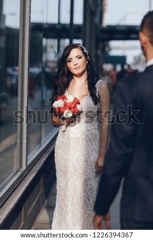 Elegant wedding couple walking in a summer city. Man in a blue suit. Woman in a white elegant dress with bouquet of roses
