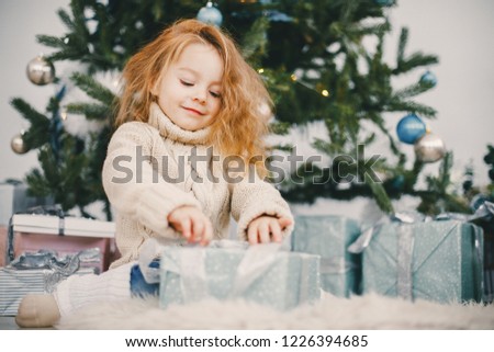 beautiful blonde todler girl opening presents next to the christmas tree