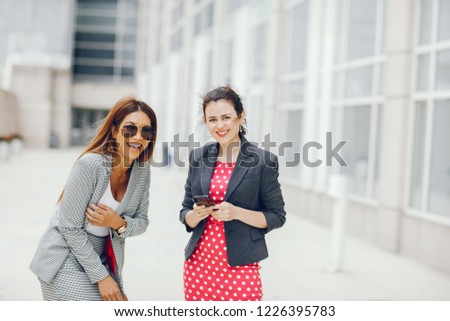 Beautiful businesswomen in a city. Businesswomen in a elegant dress. Ladies in a city. Pretty girls with phone. Two partners in a fashoin clothes