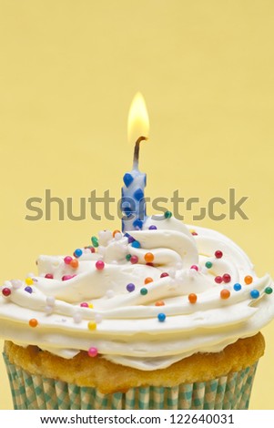 Close-up shot of a cupcake with sugar icing with burning candles over yellow background.