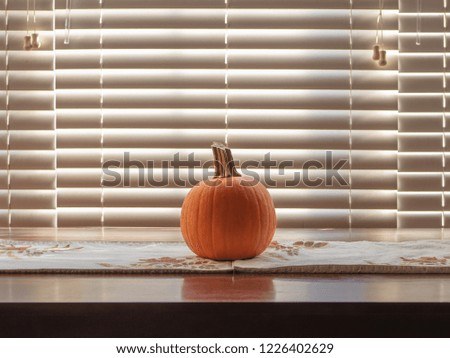 Pumpkin on a fall holidays themed placemat on top of a small brown wood table