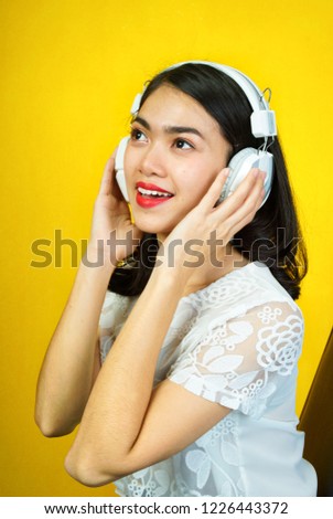 The Asian girl is listening to the happy headphones with a yellow background.