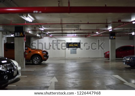Basement interior underground parking lot in a modern building with few cars parked and few space left empty. Seeing a red fire hydrant pipeline as foreground & a yellow dead end sign as background.