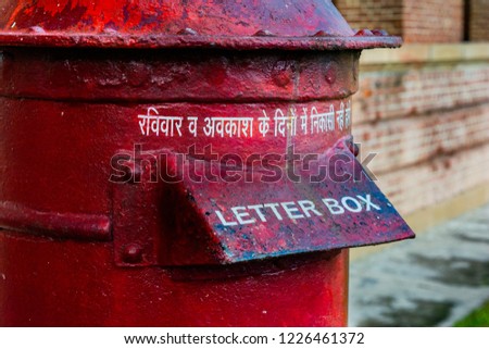 Close up picture of a red colored letter box in India with letters meaning No withdrawals will be made on off days and holidays. Picture is taken in afternoon. Letterbox looks old and is rusty. 