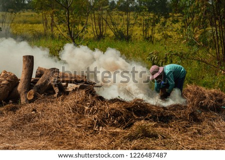 Asian guy wearing green shirt, hat and mask is creating a fire with hay. He is about to burn charcoal. It is a business that generates income for the family.
