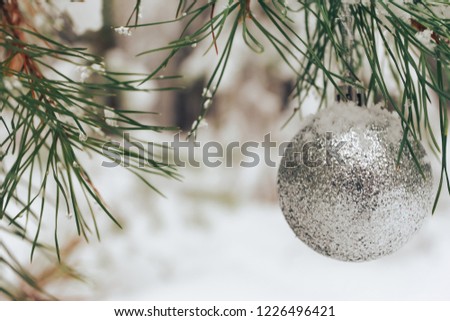 Silver Christmas bauble hanging on fir tree branch. Christmas concept. Snowy forest in blurred background. New Year, copy space, outdoors