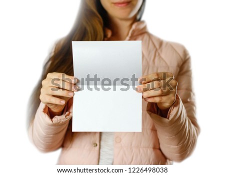 A woman in a warm winter jacket holding a white leaflet. Blank paper. Close up. Isolated on white background.